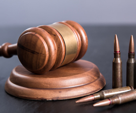 Wooden gavel and pounding block on grey background with bullet shells standing up.