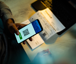 Hand holds cell phone attempting to scan a QR code on an invoice below on table